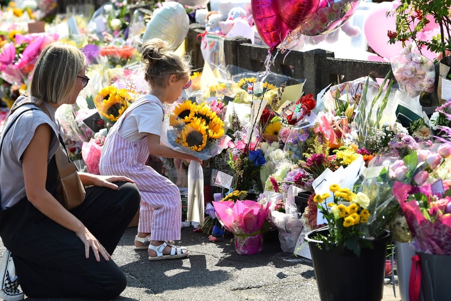 A mother looks at her child laying a bouquet of sunflowers next to floral tributes for the victims of a deadly knife attack in Southport, northwest England, on July 31, 2024.