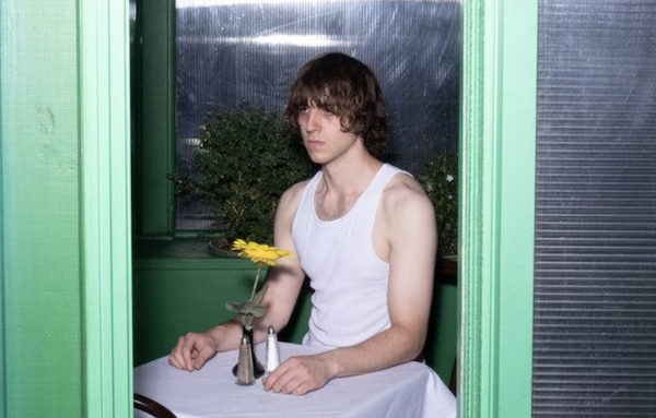 Cameron Winter sitting at a cafe-style table with a flower